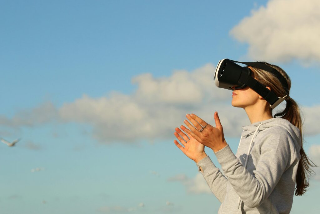 Woman using VR headset outdoors, exploring virtual reality under a clear blue sky.