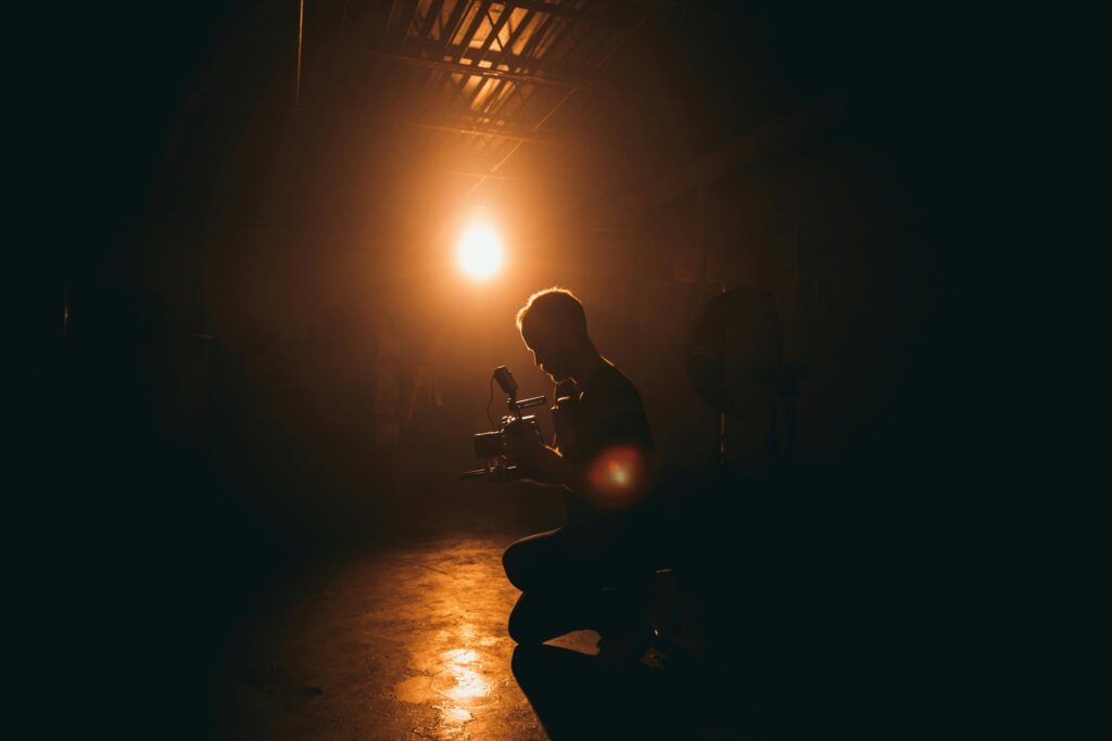 Silhouette of a cinematographer operating a camera in a dimly lit studio with dramatic lighting.