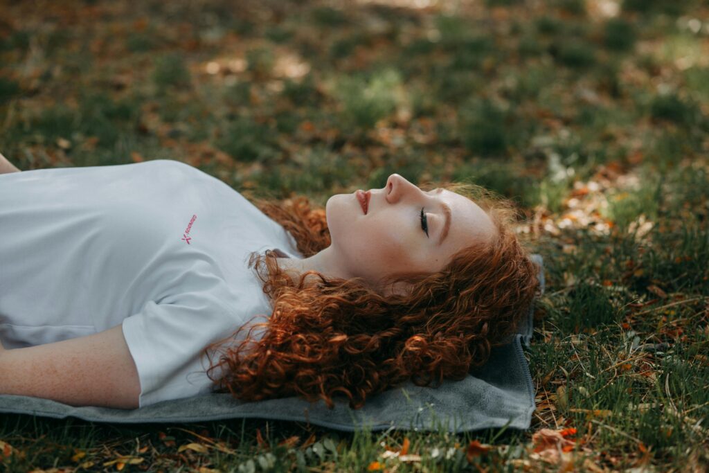 Adult woman with red hair resting peacefully outdoors on a sunny day, surrounded by nature.