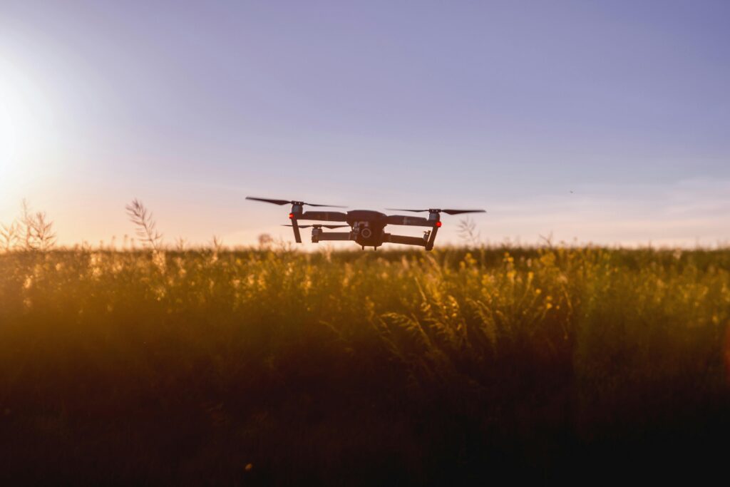 A drone flies over a field during sunset, capturing stunning aerial views.