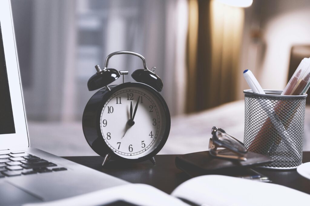 A classic analog alarm clock on a modern desk setup with a laptop and pens, creating a balanced workspace vibe.