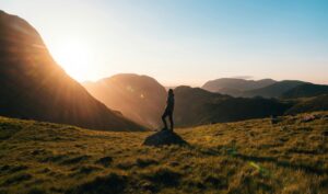 Silhouette of a person standing on a hill during sunrise in Cumbria, England with scenic mountain views.